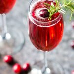 Closeup view of a mimosa garnished with a cranberry and sprig of rosemary.