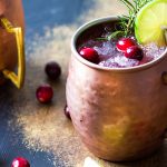 A mule cocktail in a copper mug garnished with cranberries, lime and rosemary.