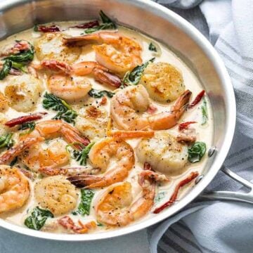 Shrimp and scallops in a cream sauce with spinach and sun-dried tomatoes in a skillet.