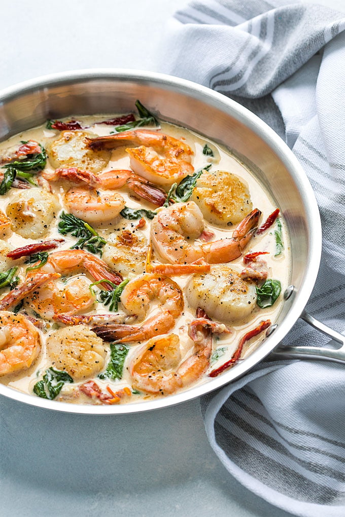 Shrimp and scallops in a cream sauce with spinach and sun-dried tomatoes in a skillet.
