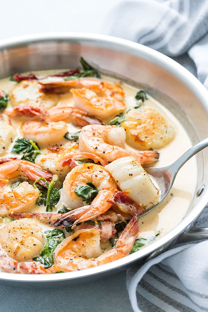 A serving spoon in a skillet of shrimp and scallops in a Tuscan cream sauce.