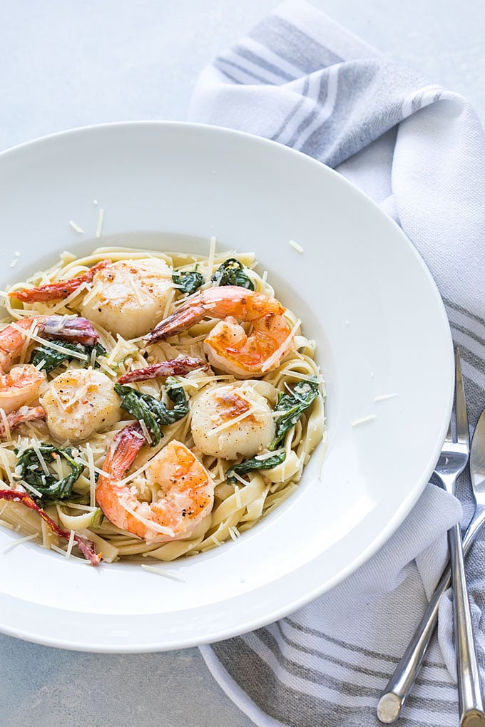 Shrimp and scallops in a Tuscan cream sauce over pasta in a white bowl.