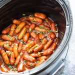 Little smokies in sauce topped with chopped parsley in an oval slow cooker.