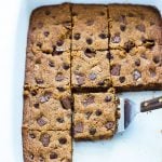 Chocolate chip bars that have been cut into squares in a baking dish with a spatula.