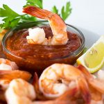 A shrimp dipped in a glass bowl of cocktail sauce.