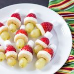Green grapes, sliced bananas, strawberries and marshmallows on toothpicks on a white plate.