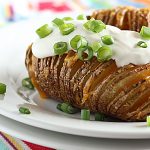 Front view of hasselback potatoes topped with sour cream and green onions on a white plate.