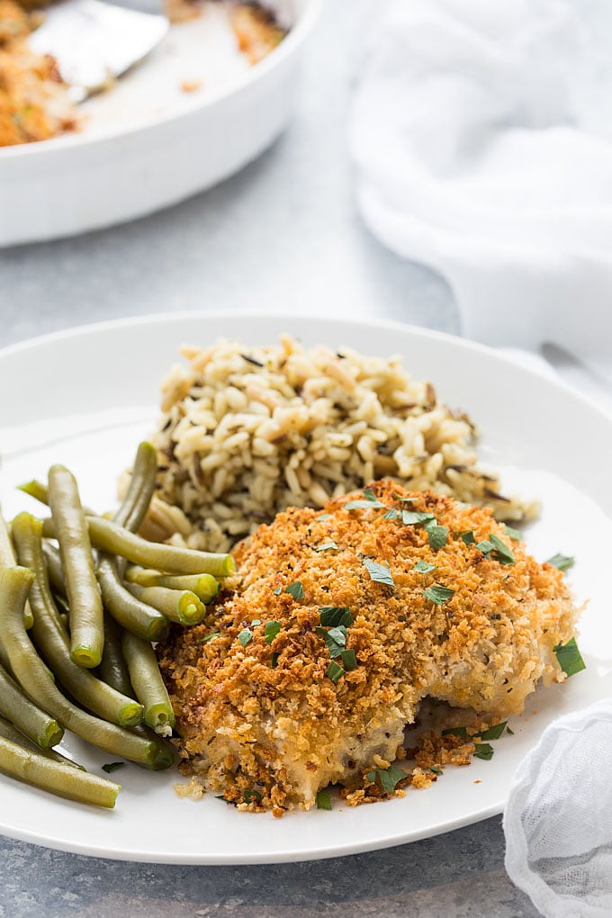 An herb breaded chicken thigh, rice and green beans on a white plate.