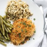 Overhead view of a piece of breaded chicken, rice and green beans on a white plate.