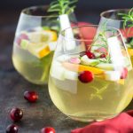 Front view of three glasses of white sangria with cranberries, apples, oranges and rosemary.