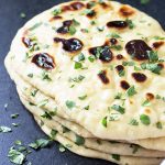 A stack of naan bread sprinkled with chopped parsley by a striped kitchen towel.