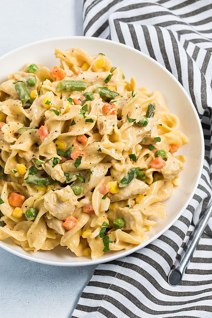 Overhead view of cheesy egg noodles with chicken and vegetables in a white bowl.