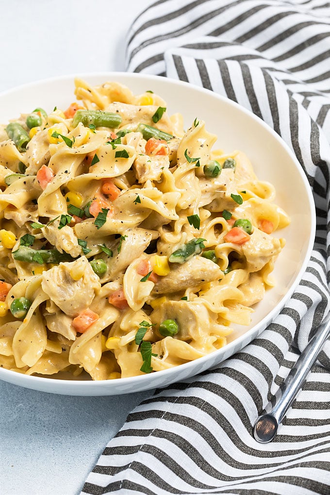 A bowl of cheesy noodles with chicken and vegetables by a striped napkin and a fork.
