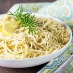 A white bowl of pasta topped with lemon and rosemary by a patterned napkin.