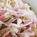 A closeup of coleslaw with onions and green peppers in a white bowl.