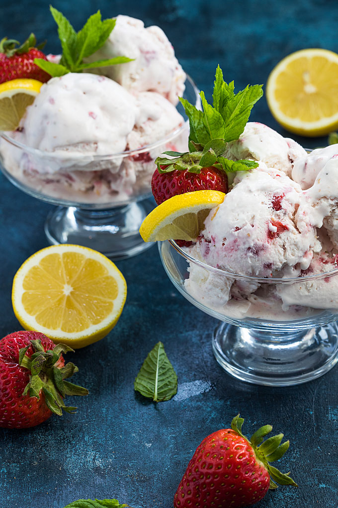 Two glass bowls of strawberry lemon ice cream on a blue surface.