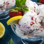 Closeup of strawberry lemon ice cream in a glass bowl on a blue surface.
