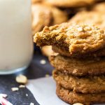A stack of cookies on a piece of parchment paper by a glass of milk.