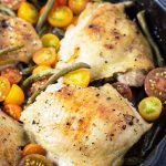A closeup of roasted chicken with tomatoes and green beans in a cast iron skillet.