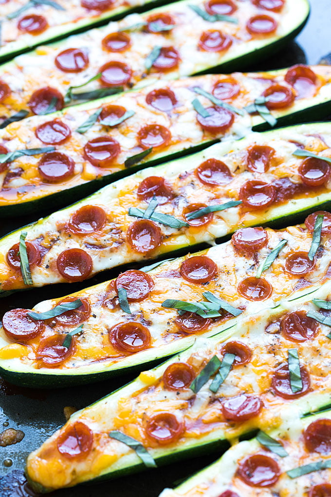 A closeup of zucchini boats with cheese, pepperoni and basil on a baking sheet.