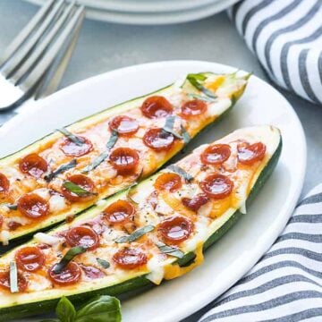 Two zucchini pizza boats on an oval white plate by a striped napkin.