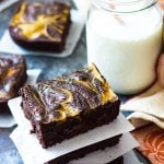 Three stacked brownies by a glass of milk with a straw.