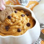 A cookie being dipped into a white bowl of pumpkin dip.