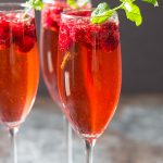 Front view of three flutes of champagne punch with raspberries and mint sprigs.