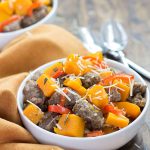 Crumbled sausage, squash and peppers in a white bowl beside an orange napkin.