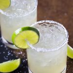 Two margaritas in salted rim glasses garnished with lime wheels.