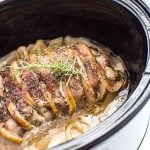 A sliced cooked pork loin with apples and rosemary in an oval slow cooker.