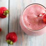 Overhead view of a smoothie in a glass with a straw and garnished with a strawberry.
