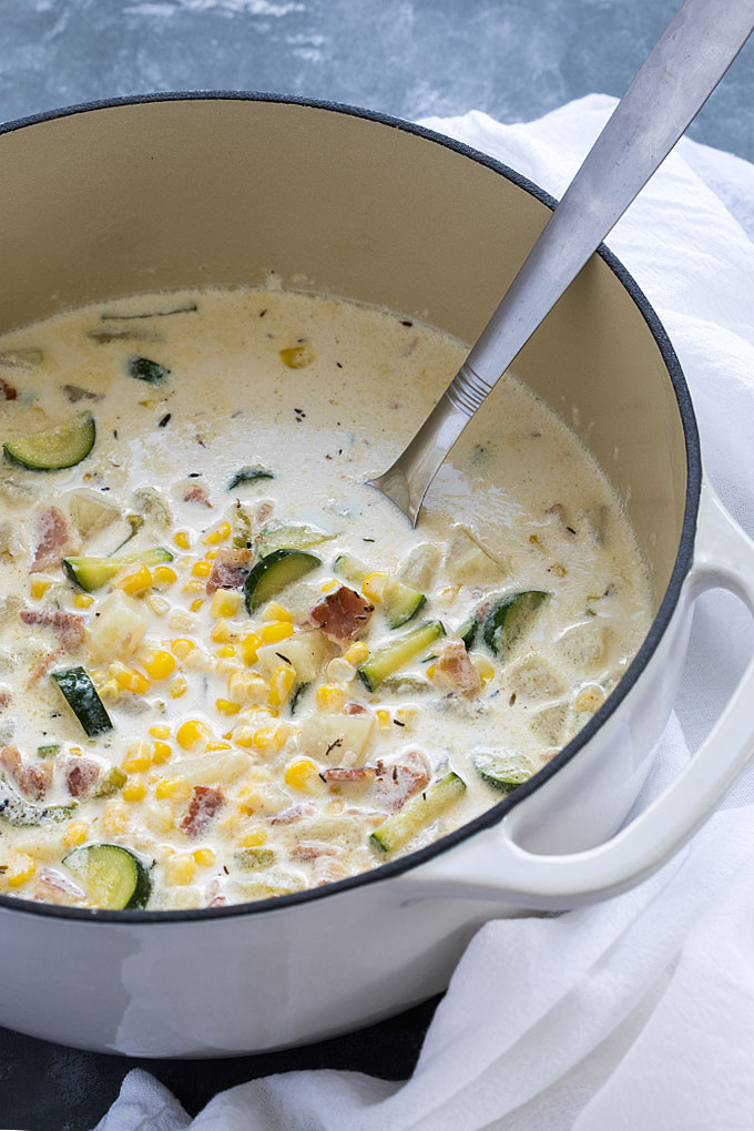 Corn and zucchini chowder in a white Dutch oven with a ladle.