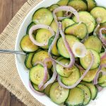 Overhead view of cooked zucchini squash and red onions in a white bowl with a spoon.