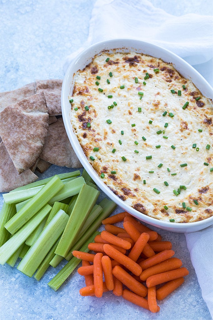 Overhead view of crab dip in a baking dish beside pita bread, celery and carrots.