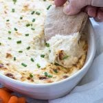 A hand dipping a piece of pita bread into a dish of crab dip.