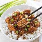 Mongolian chicken topped with green onions over rice in a  bowl with a pair of chopsticks.