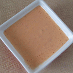 Overhead view of red pepper sauce in a square white bowl.