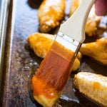 Brushing wing sauce on a chicken wing in a baking pan.