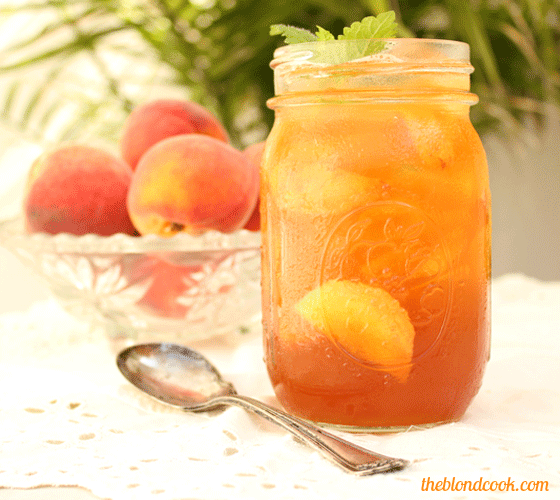Front view of a mason jar of peach tea cocktail by a spoon.