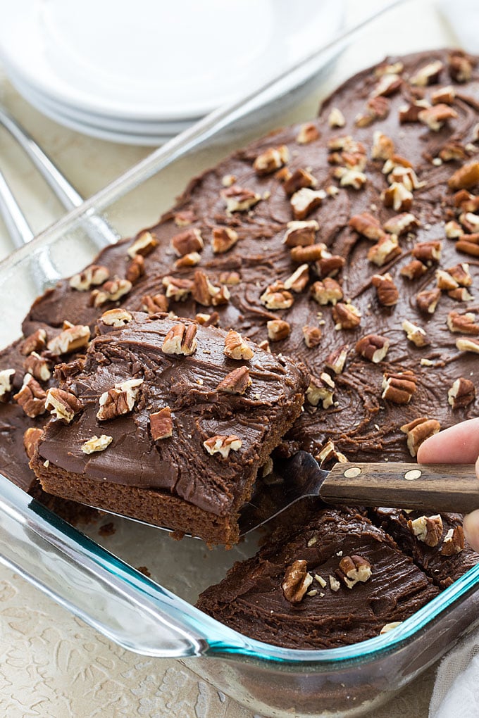 A spatula removing a slice of chocolate cake with pecans from a baking dish.
