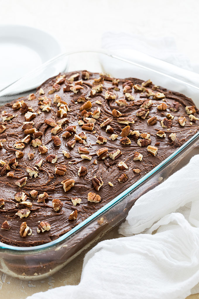 A chocolate cake topped with pecans in a glass baking dish.