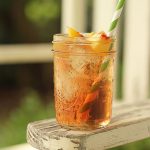 A whiskey cocktail in a small mason jar with a straw sitting on a rocking chair arm.