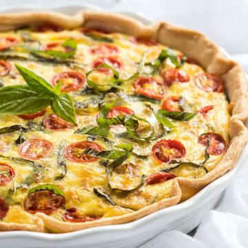Front view of a quiche with tomatoes and basil in a white pie dish.