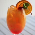 Front view of a cocktail garnished with lime, orange and a cherry.