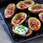 Baked potato skins topped with cheese, bacon and sour cream on a baking sheet.