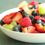 Fruit salad in a white bowl on a green surface.