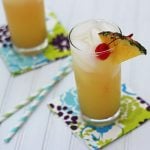 A pineapple cocktail in a glass on a patterned napkin by two straws.