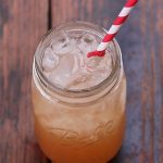 A cocktail in a mason jar with a striped paper straw on a wood surface.
