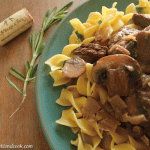Overhead closeup view of beef and mushrooms over noodles in a teal plate.